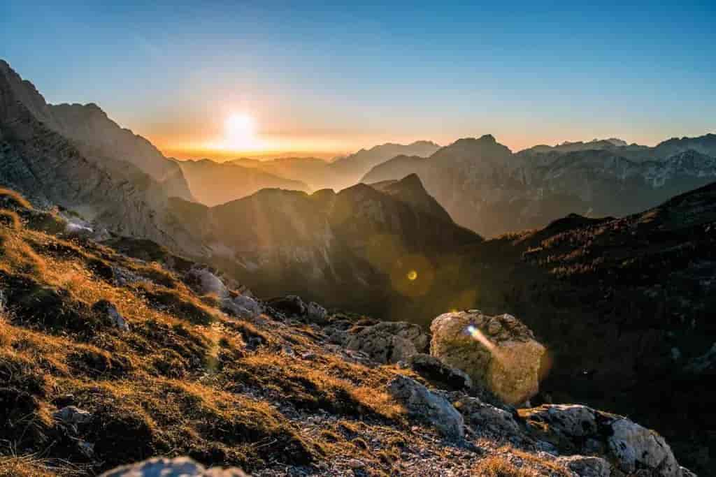 Mountain landscape at sunset with sun flare over rocky, grassy foreground near Prehodavci.