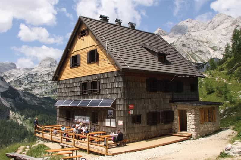 Vodnik's Hut (Vodnikov dom) with wooden exterior and terrace against rocky alpine mountains.