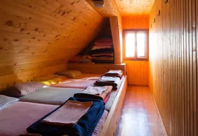 Attic dormitory room with wooden walls, built-in beds, and bright window light, Prešernova Koča na Stolu.