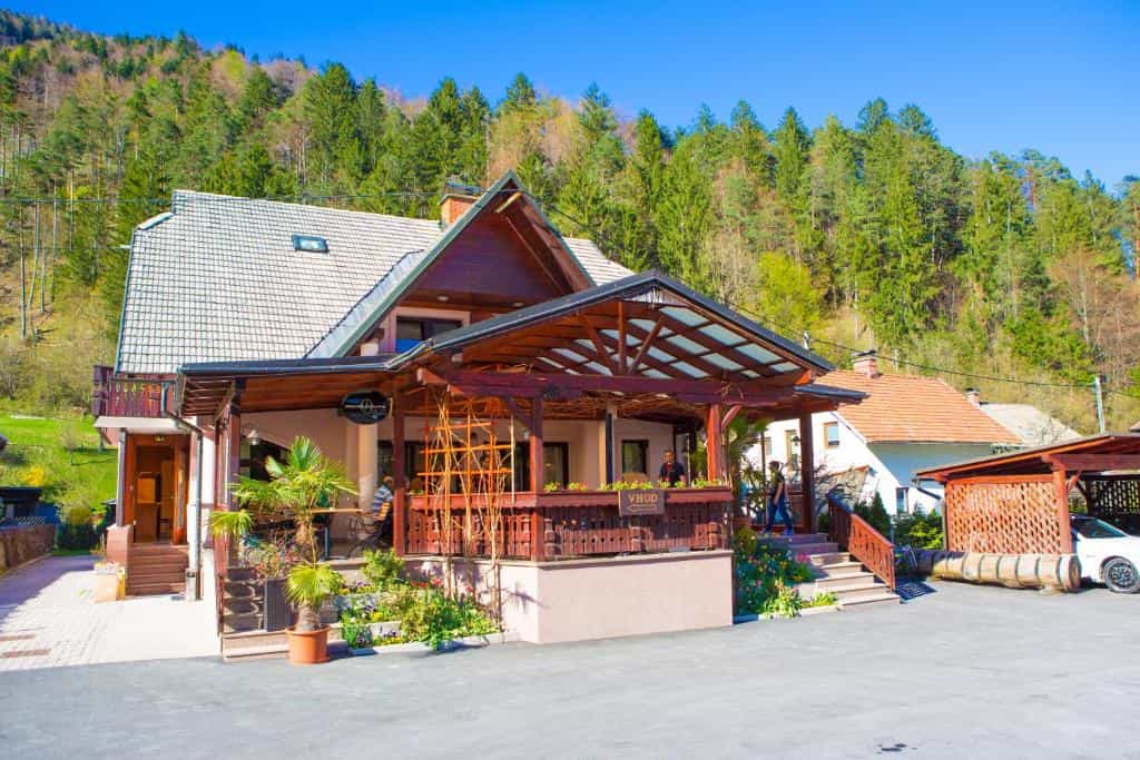 Guesthouse veranda with wooden structure against a steep, forested hillside under blue sky
