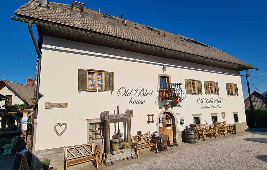 Old Bled House restaurant exterior with wooden press, benches, and clear blue sky.