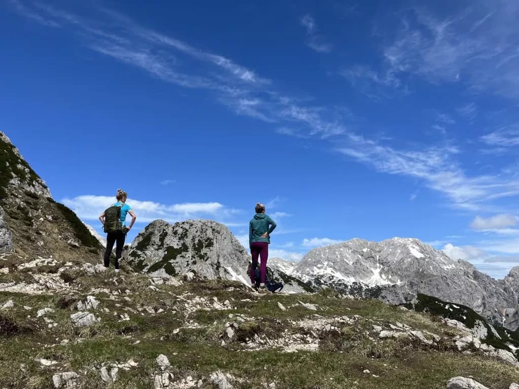 Hikers overlooking rocky mountains with snow patches under a bright blue sky near Viševnik.