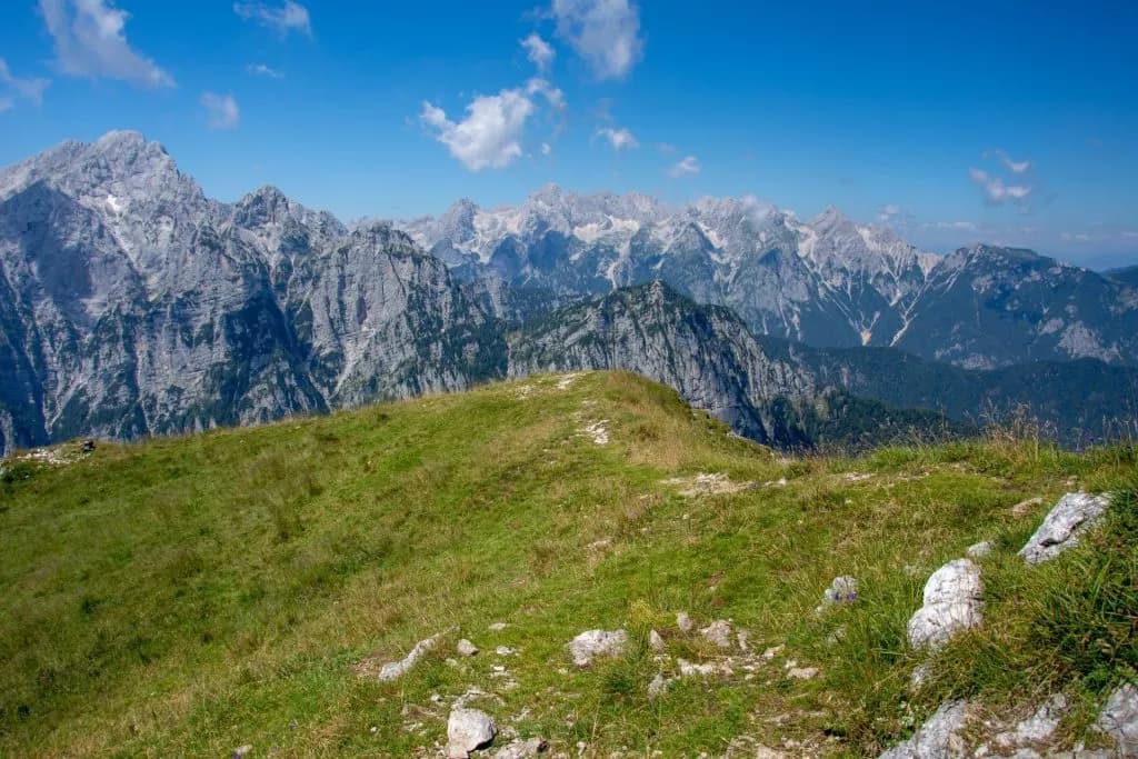 Grassy mountain ridge trail overlooking rugged, rocky peaks under a bright blue sky.