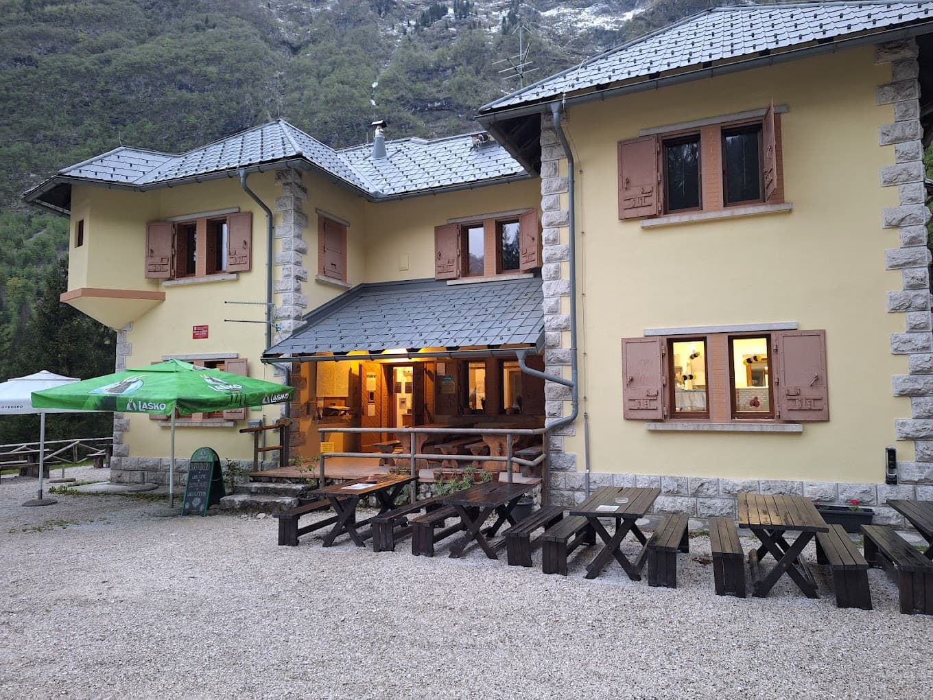 Mountain hut with outdoor picnic tables and green umbrella at Dom Klementa Juga v Lepeni.