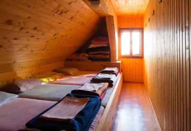 Attic dormitory room with wooden walls, built-in beds, and bright window light, Prešernova Koča na Stolu.
