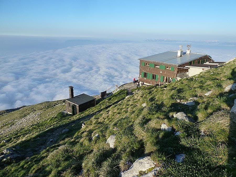 Mountain hut above a sea of clouds on a grassy slope, Prešernova Koča na Stolu.