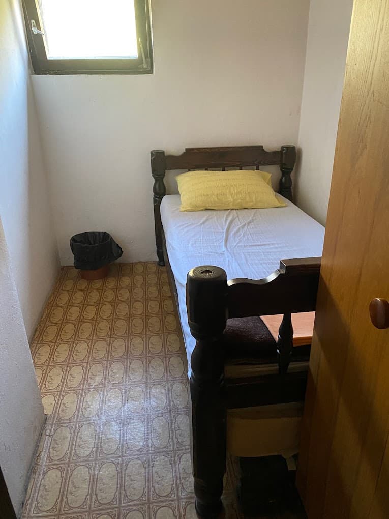 Small bedroom with single dark wood bed, yellow pillow, and small window.