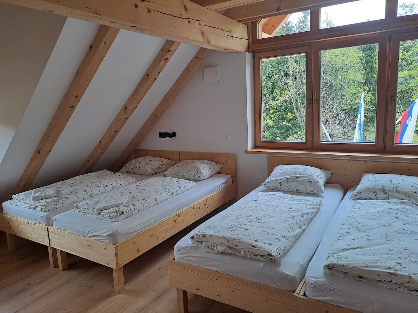 Attic bedroom with wooden beds and window view of green trees at Planinska koča na Uskovnici.