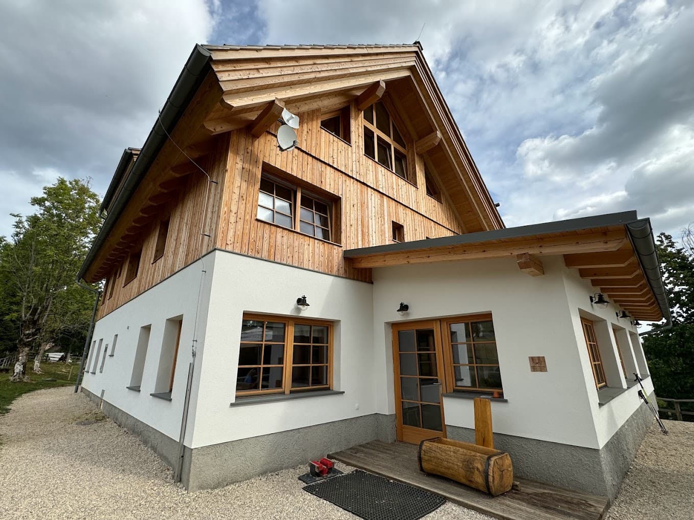 Planinska koča na Uskovnici mountain hut with white stucco and wood siding under cloudy sky.