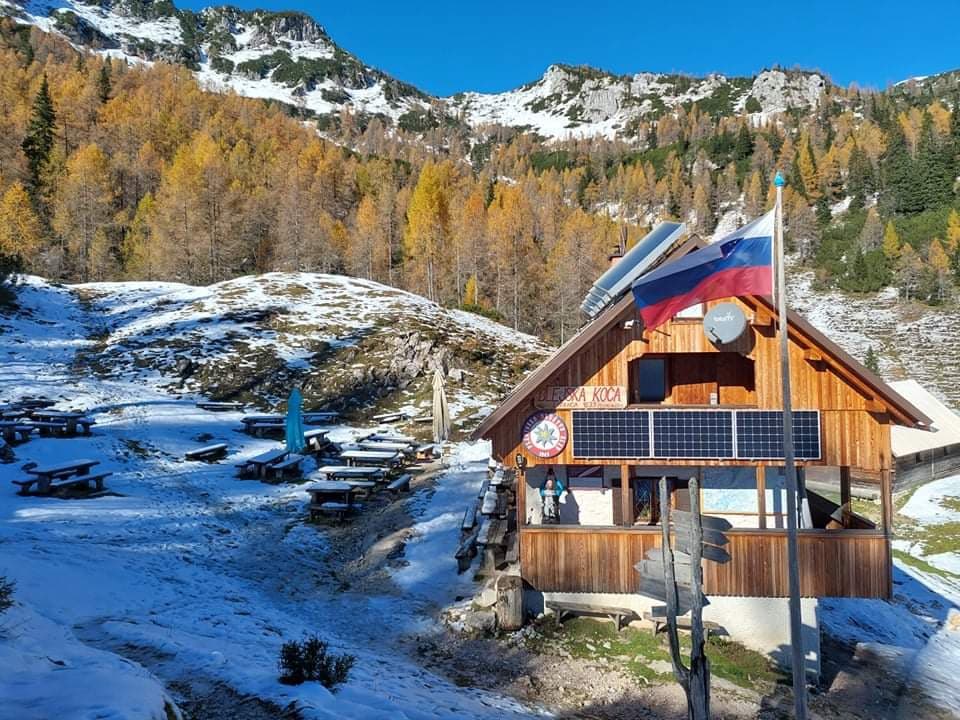 Blejska koča na Lipanci mountain hut with Slovenian flag, autumn trees, and early snow.