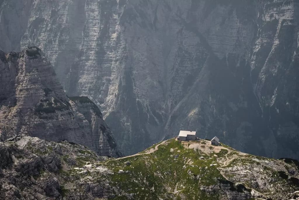 Pogačnik hut on Kriški Podi mountain ridge with steep gray peaks in the background.