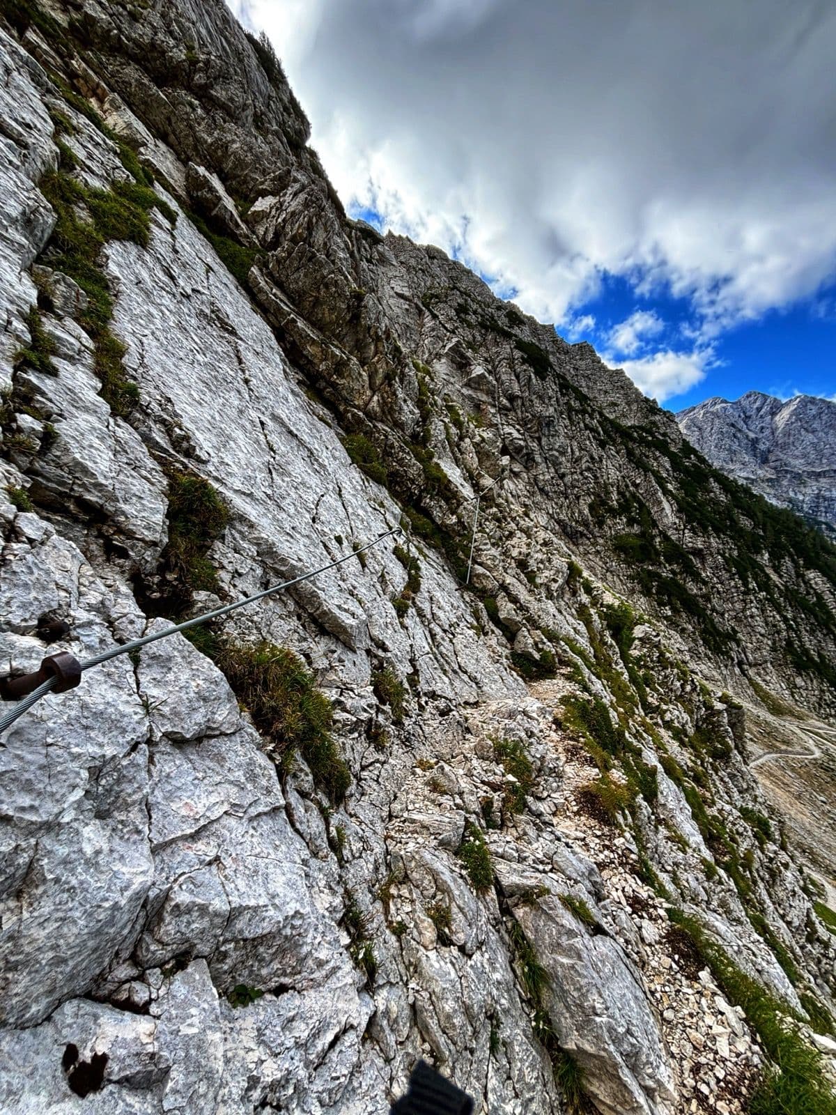 Via ferrata climbing route with steel cable on a steep rocky mountain face.