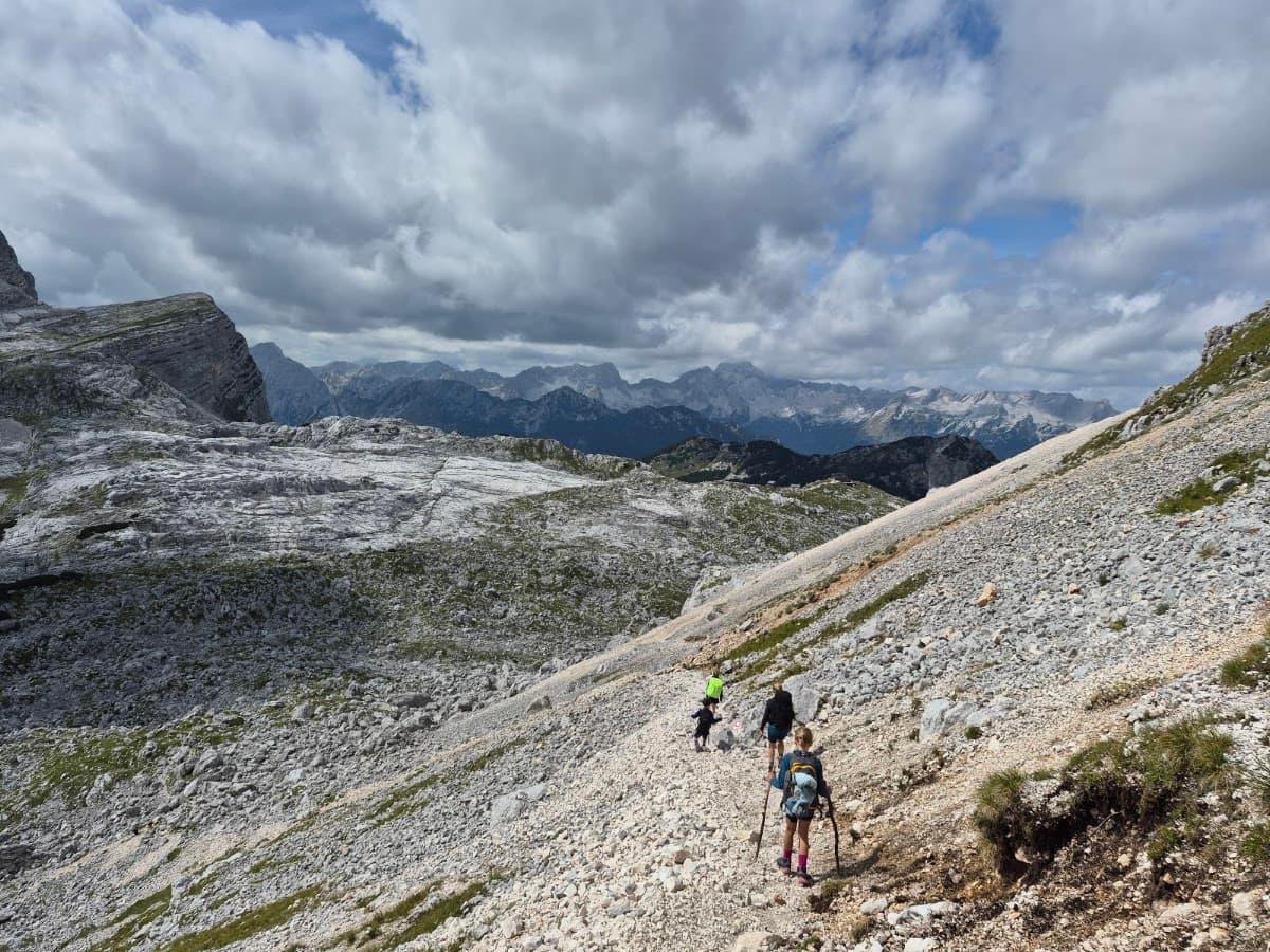 Hikers walking on a rocky mountain trail under a cloudy sky