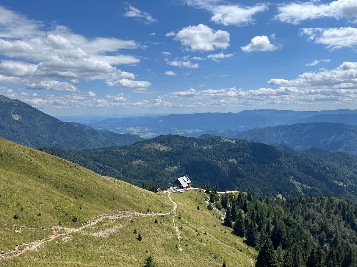 Alpine mountain landscape with a solitary cabin and hiking trail under a blue sky with clouds