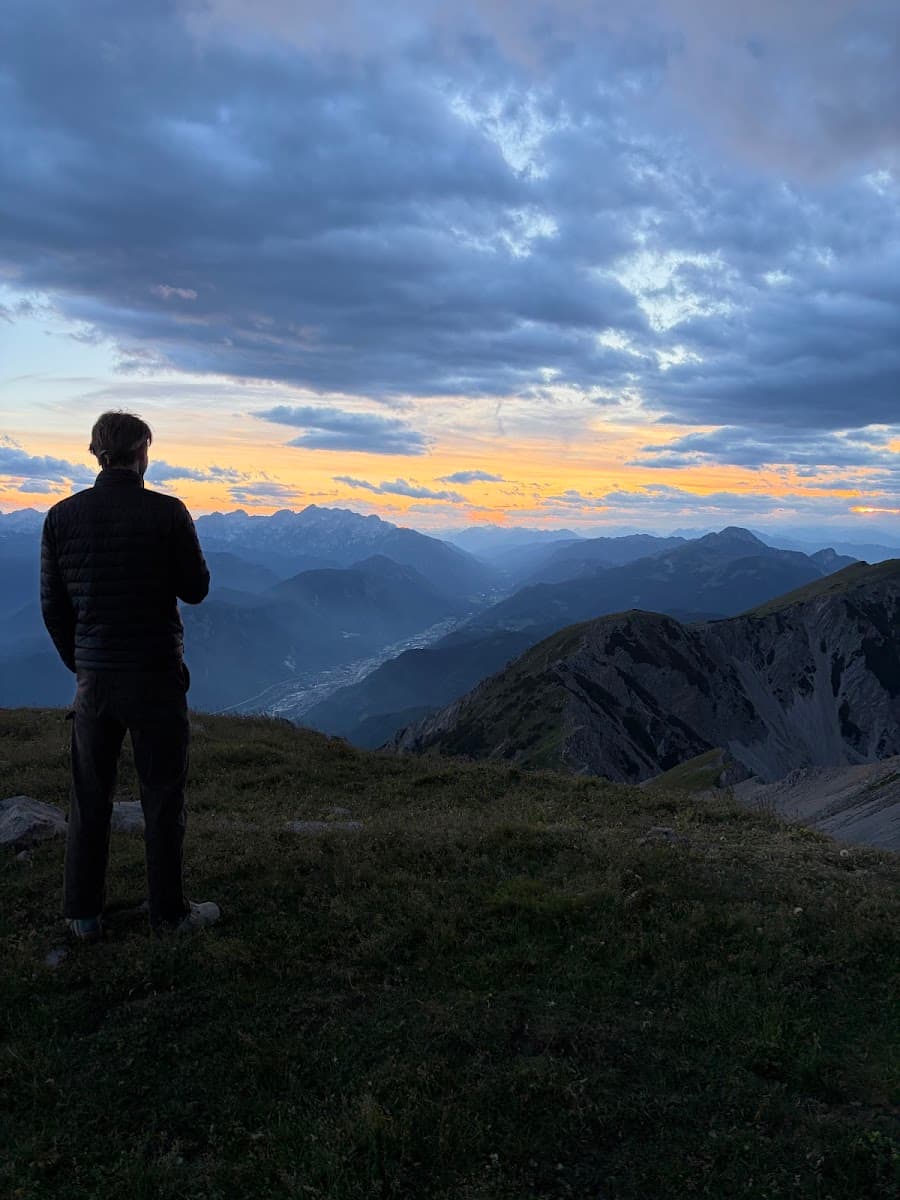 Hiker standing on mountain summit looking at sunset over alpine valley