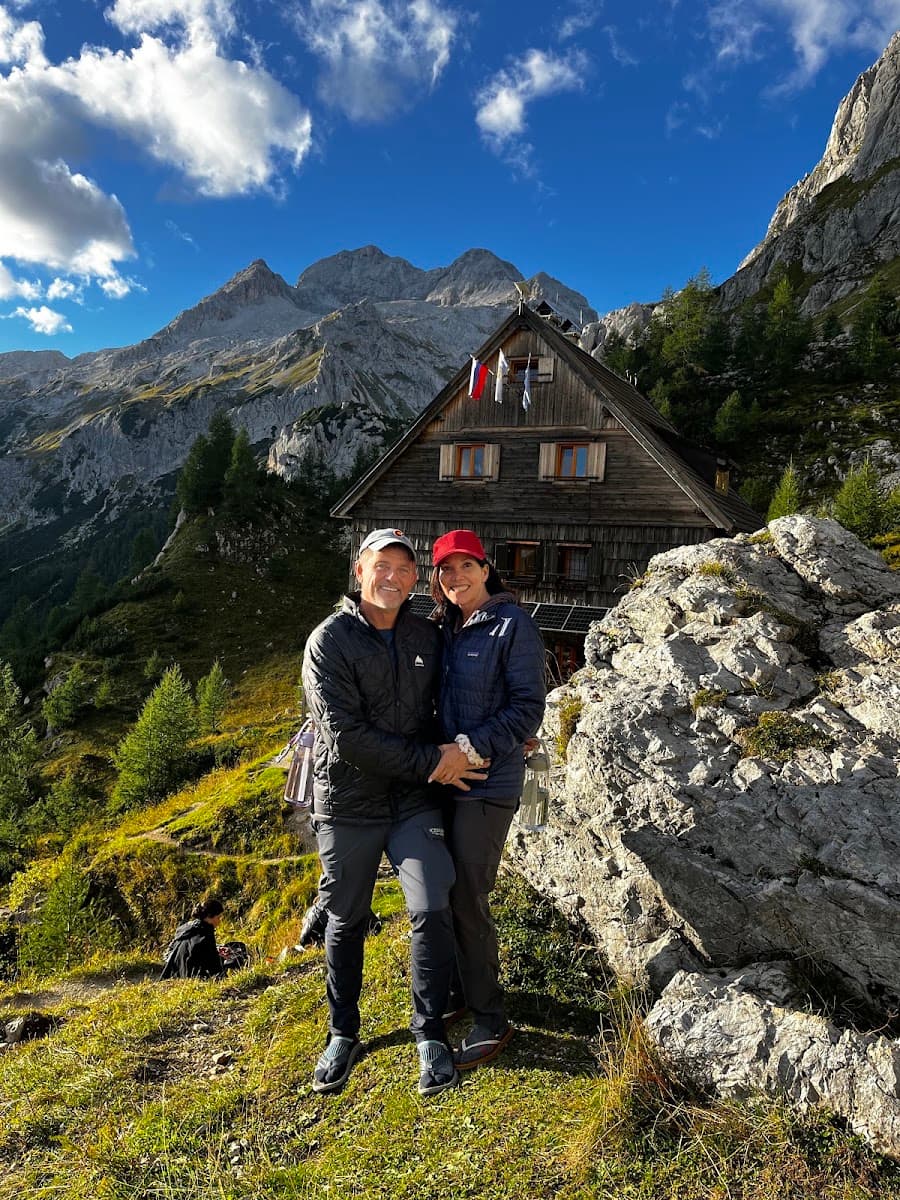 Hikers posing in front of an alpine mountain hut with rocky peaks and pine forest
