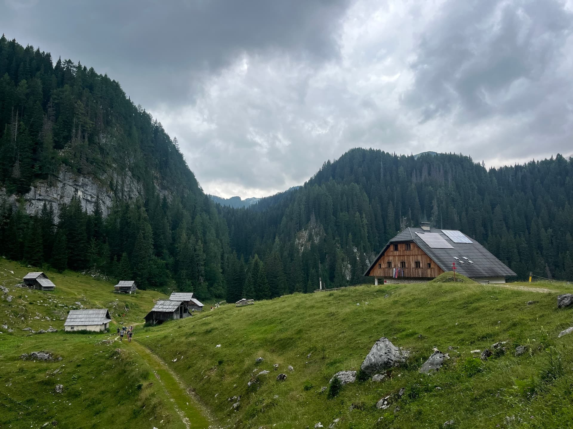 Wooden pasture huts in Julian Alps valley with forest and cloudy sky