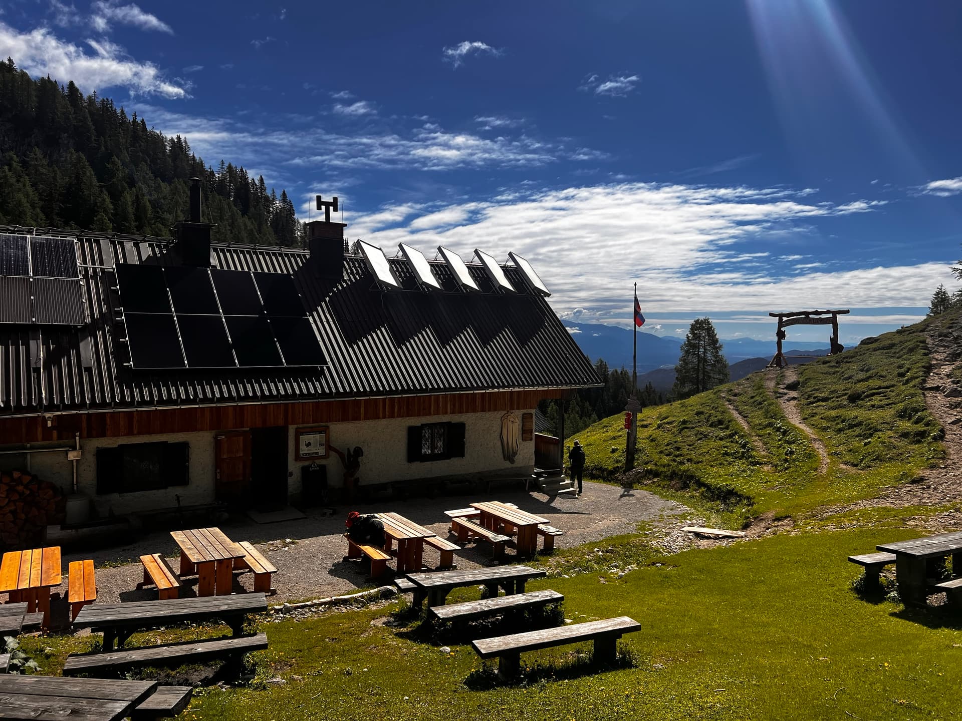 Mountain hut terrace with wooden picnic benches and solar panels under a blue sky