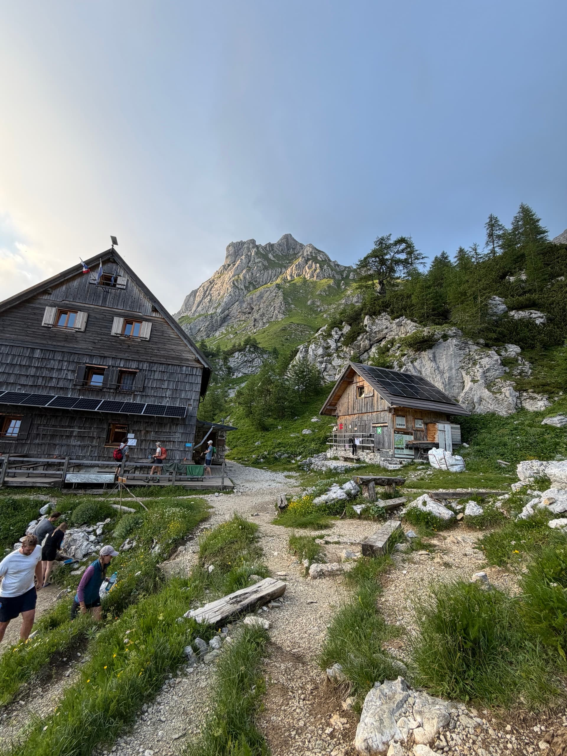 Hikers on alpine path near wooden mountain huts with rocky peaks in background