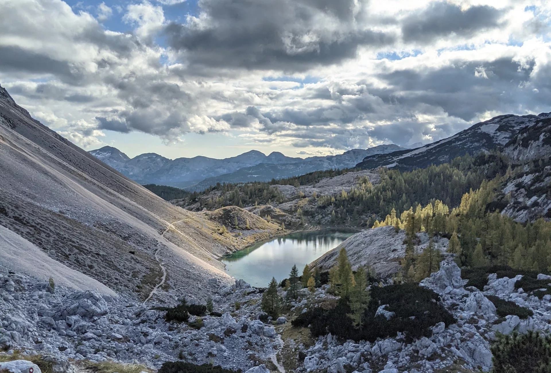 Alpine lake nestled in rocky valley with autumn trees under dramatic clouds