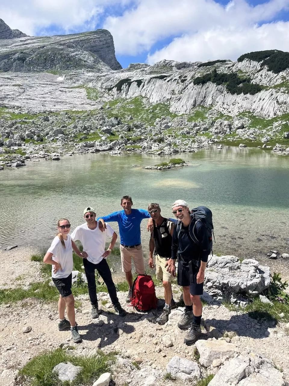 Hikers posing by Rjavo Jezero at the Seven Lakes Valley with rocky mountains and clear water.