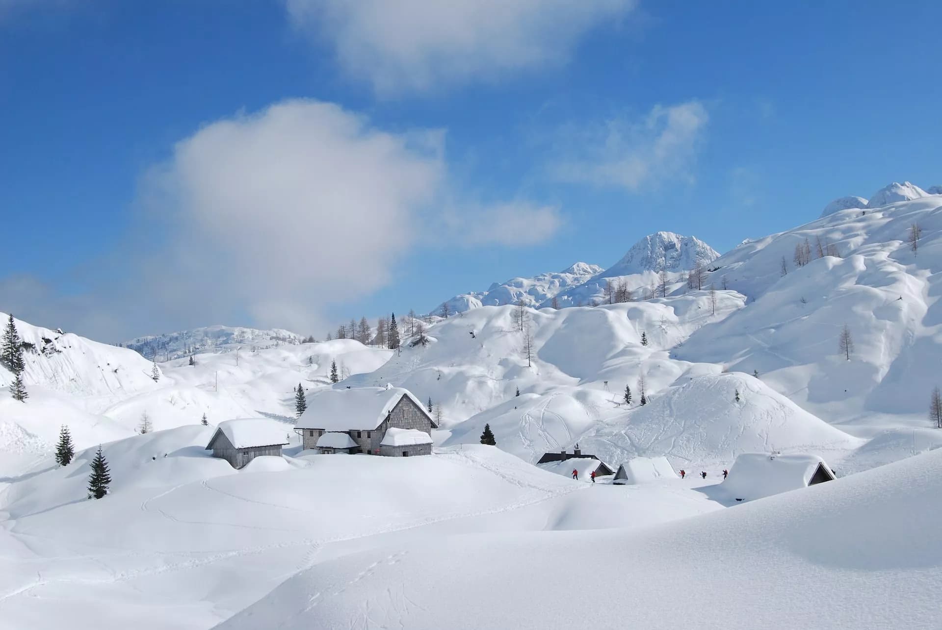 Snow-covered alpine huts below high, bright mountains under a blue sky in winter.