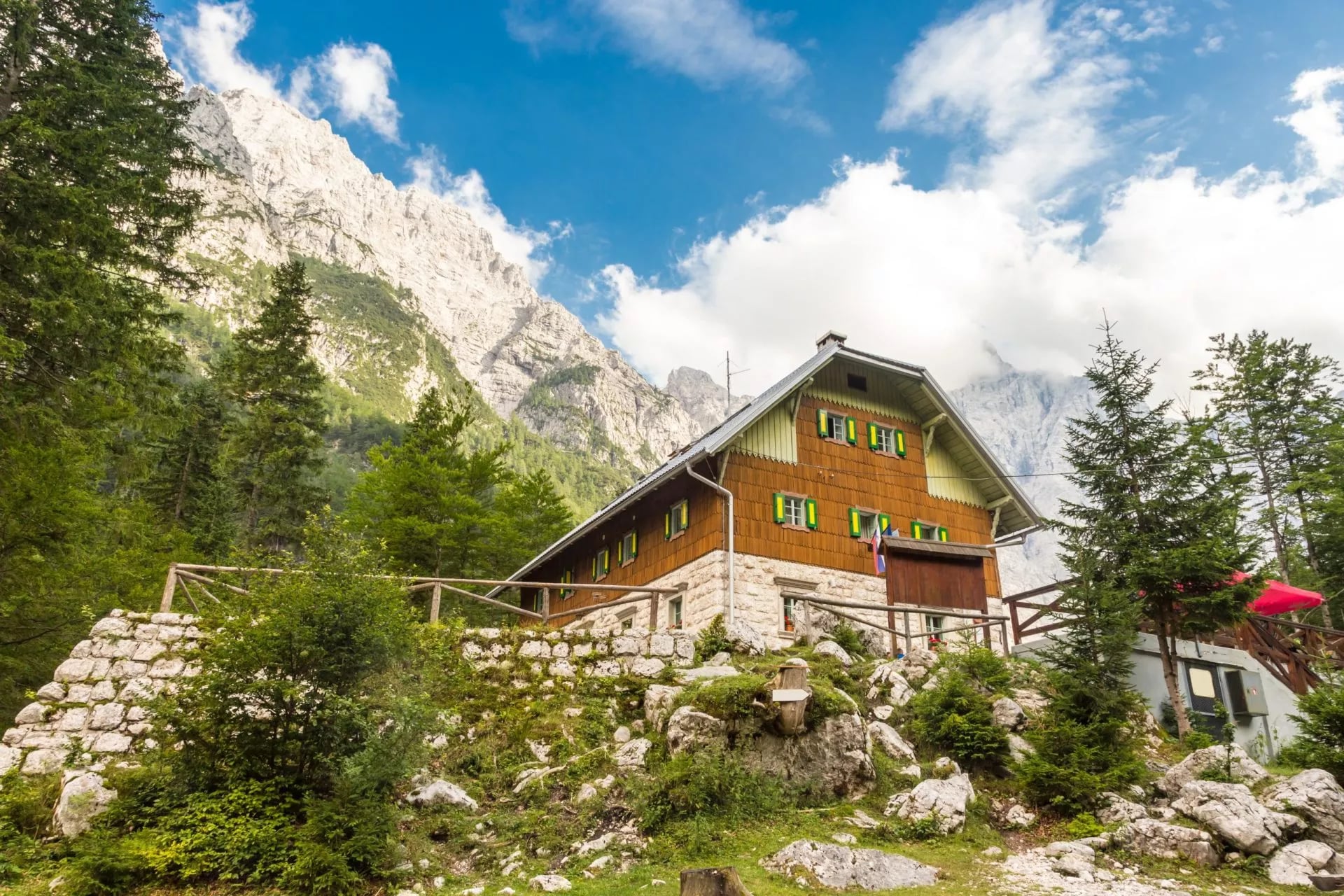 Aljažev dom mountain hut nestled below towering, rocky mountains and green pine forest