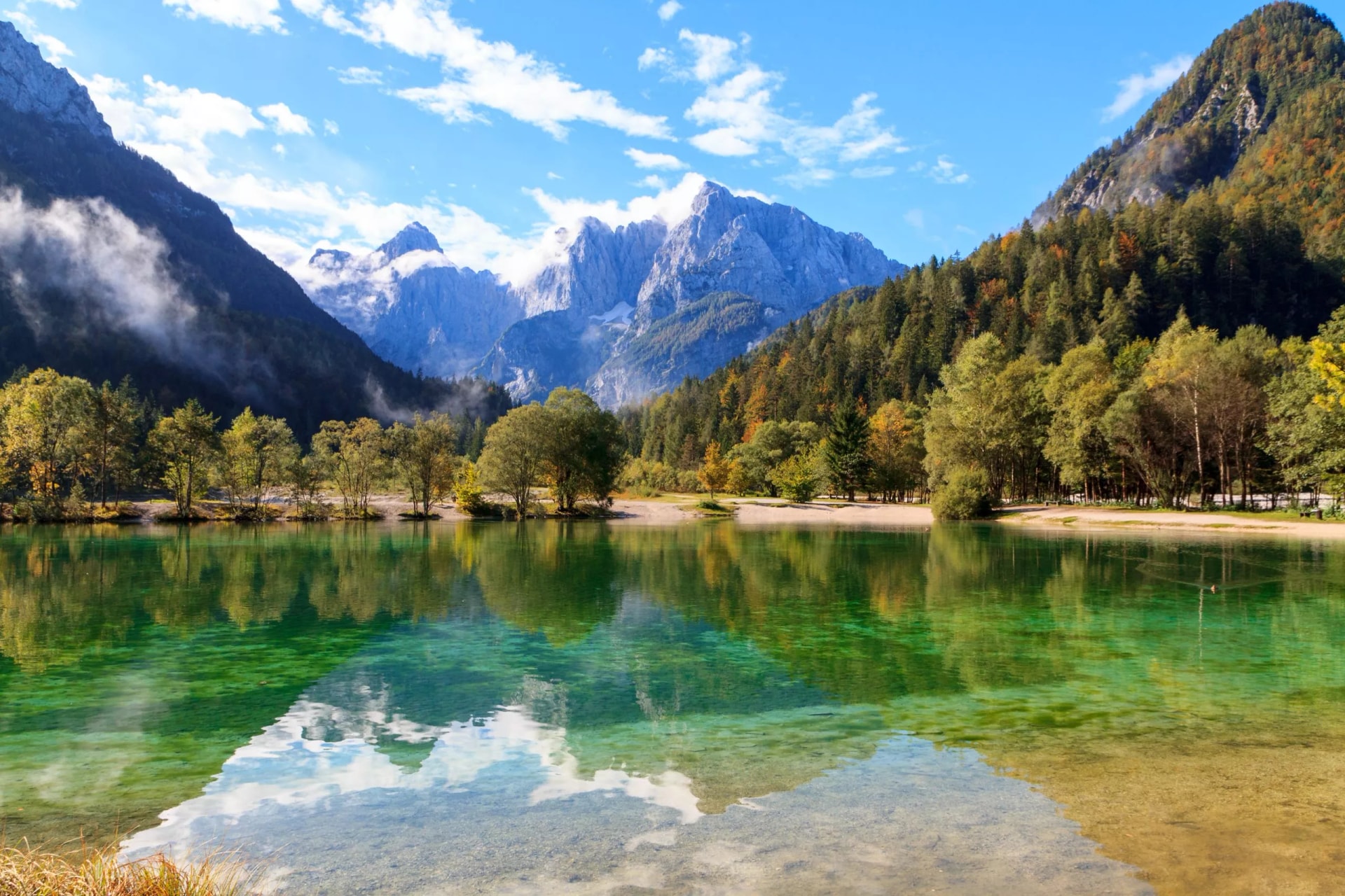 Jasna lake in Kranjska Gora, Slovenia, with emerald water reflecting autumn trees and jagged mountains.