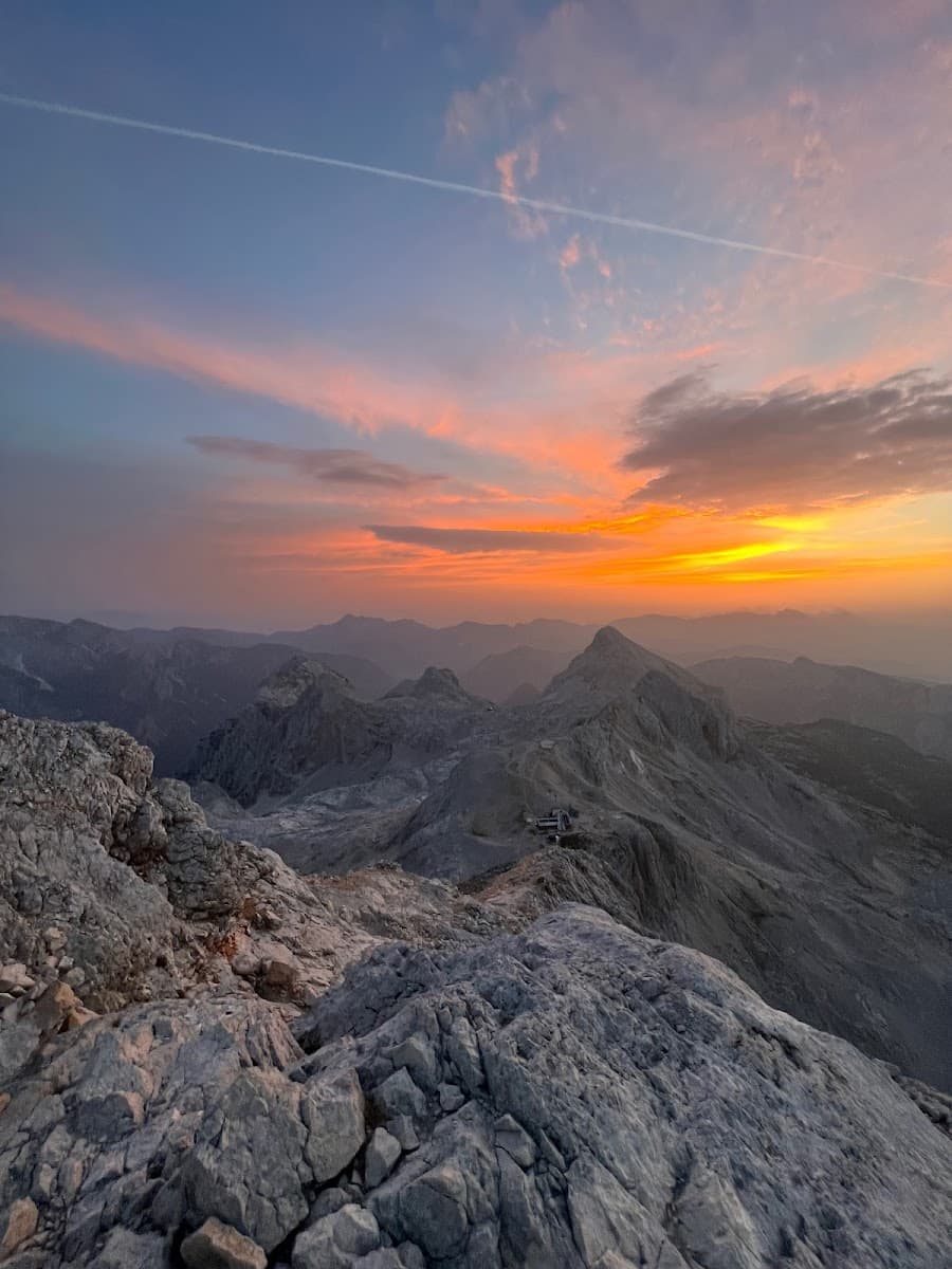 Rocky mountain landscape at sunrise or sunset with orange and pink clouds and a distant building.