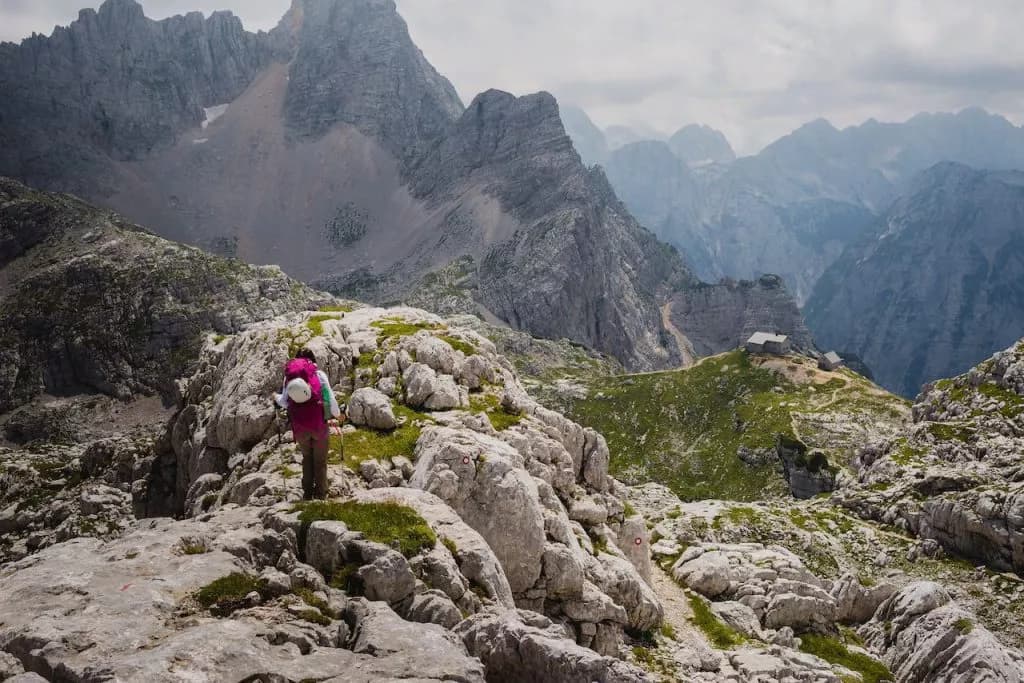 Hiker on rocky trail approaching Kriški Podi Lodge in Julian Alps mountains.