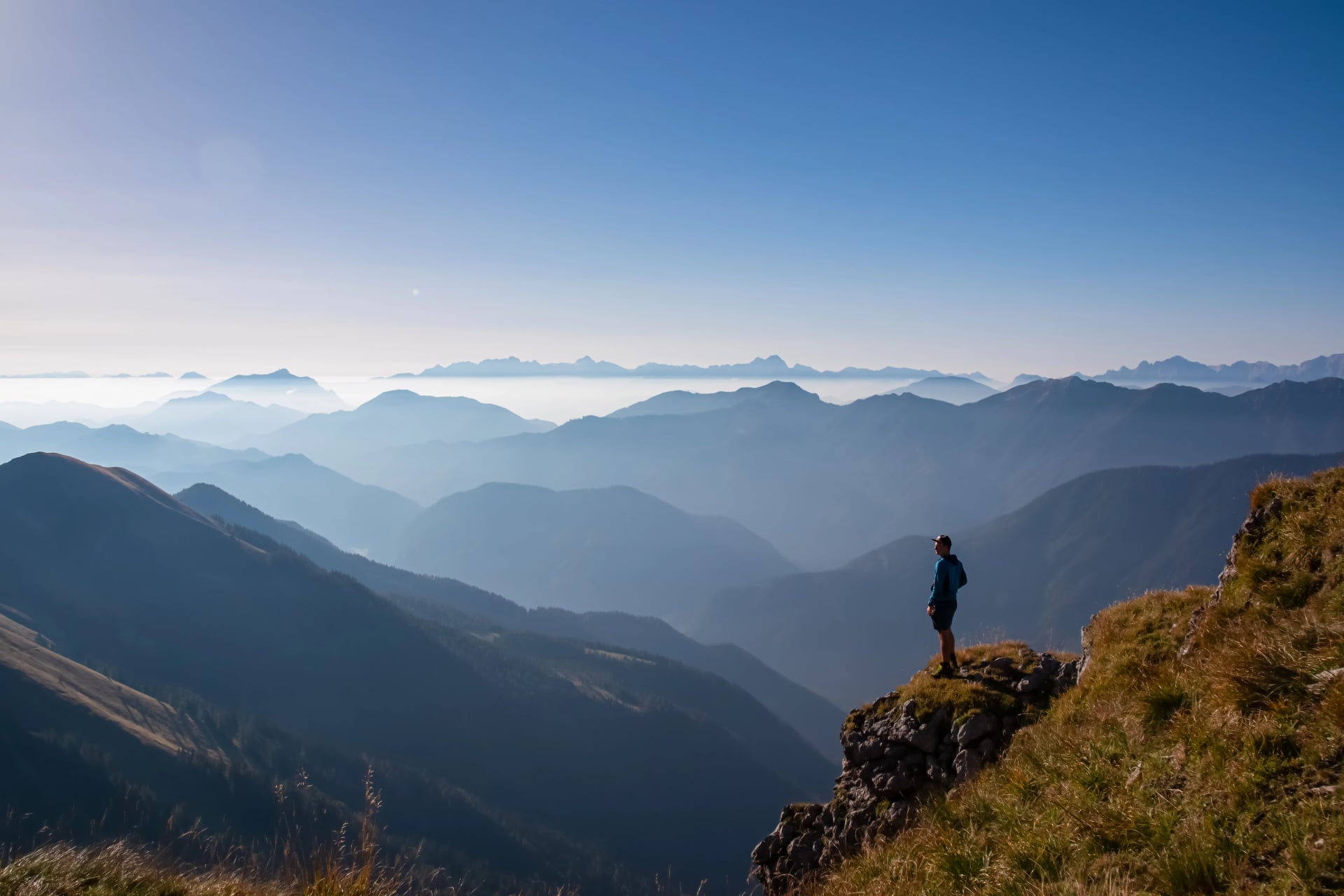 Silhouette of hiker man in alpine landscape of Gailtal Alps, Carinthia, Austria. Panoramic view of majestic hazy mountain ridges of Julian Alps, Karawanks, Carnic Alps. Peaceful tranquil atmosphere