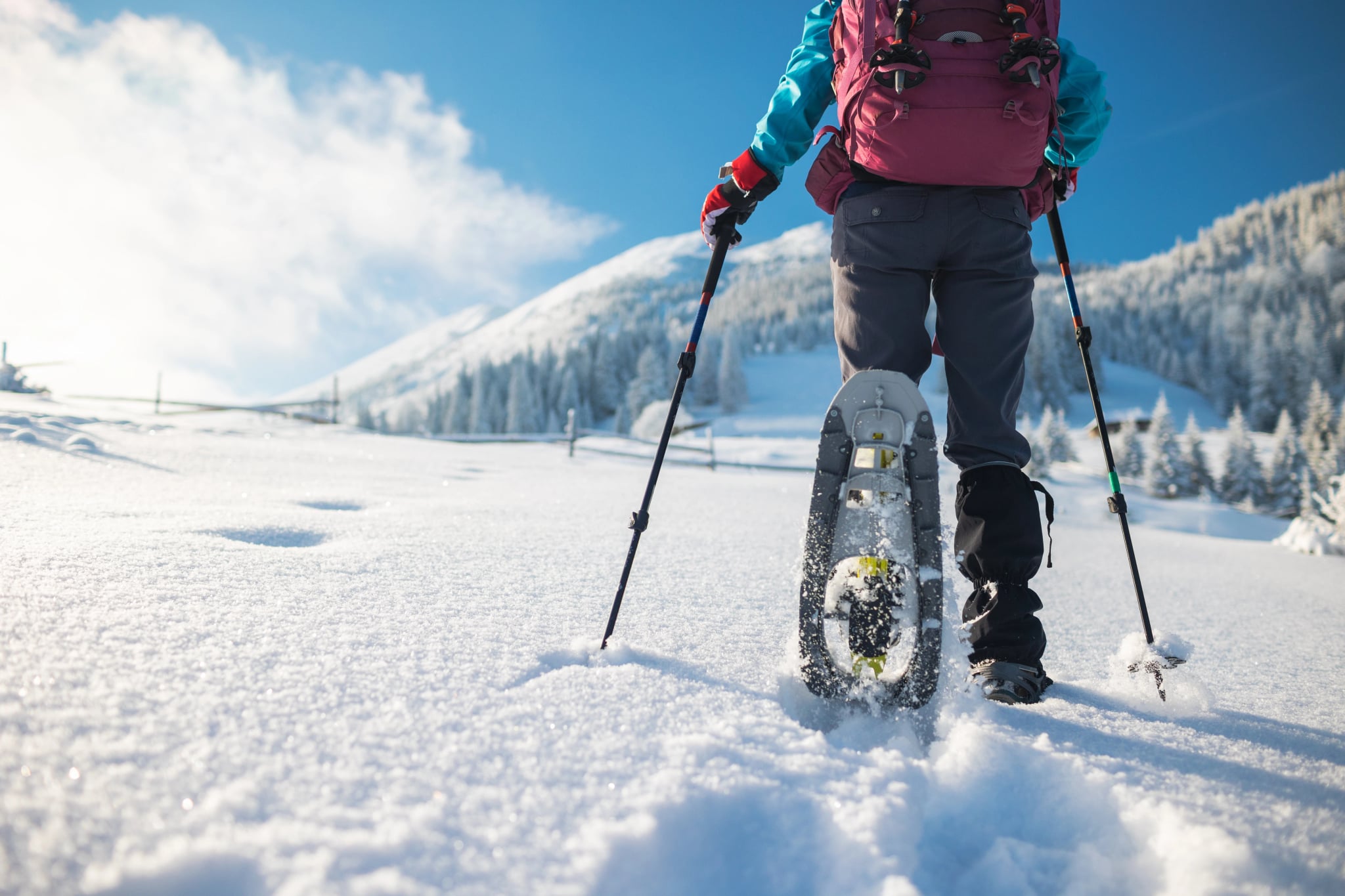 A woman with a backpack in snowshoes climbs a snowy mountain