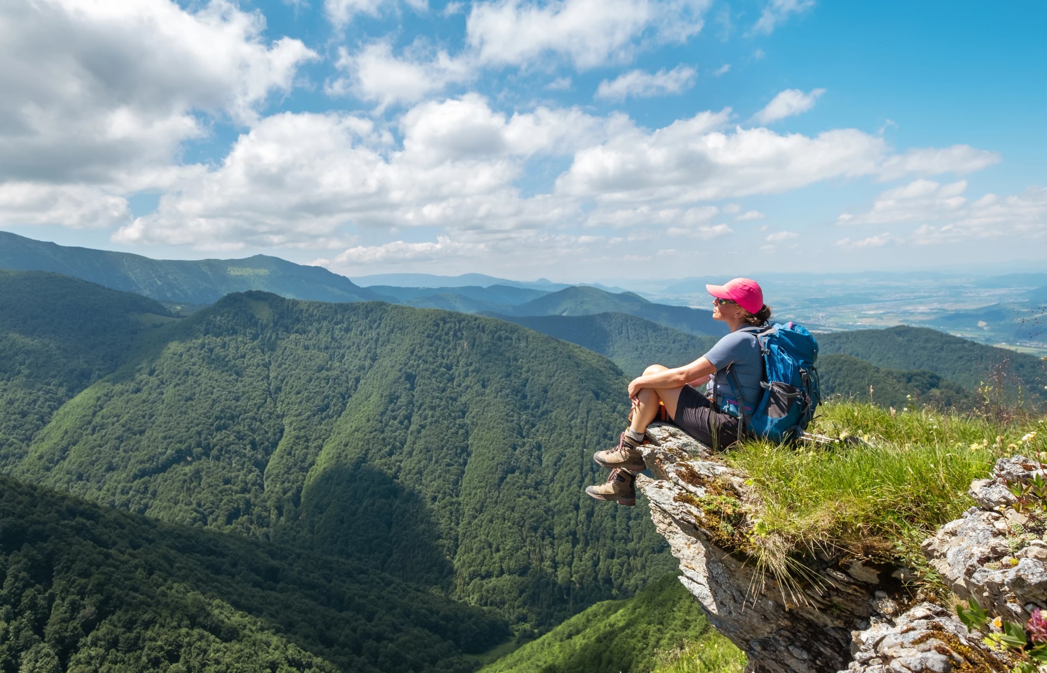 Dressed trekking clothes hiker woman sitting on rocky cliff enjoying green valley at Mala Fatra mountain range, Slovakia. Active people and European tourism concept image.