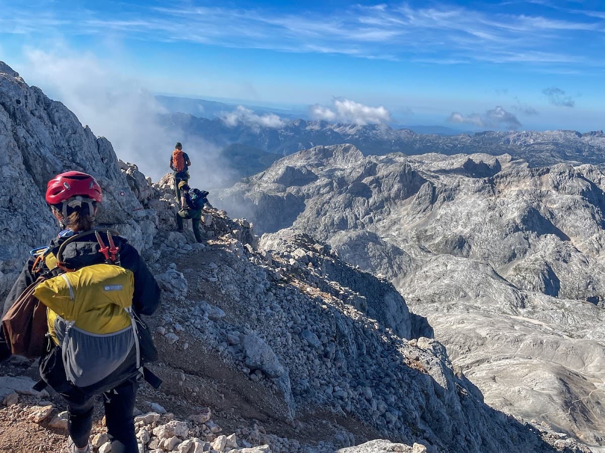 Hikers with backpacks on a rocky mountain ridge with clouds and distant peaks