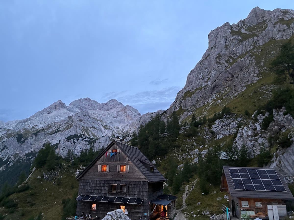 Wooden mountain hut with glowing windows beneath rocky alpine peaks