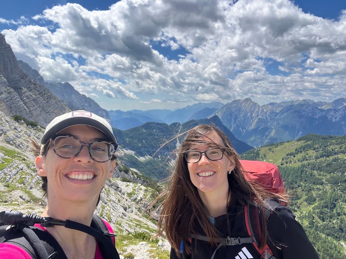 Hikers taking a selfie on a mountain summit with rocky peaks and cloudy sky in the background