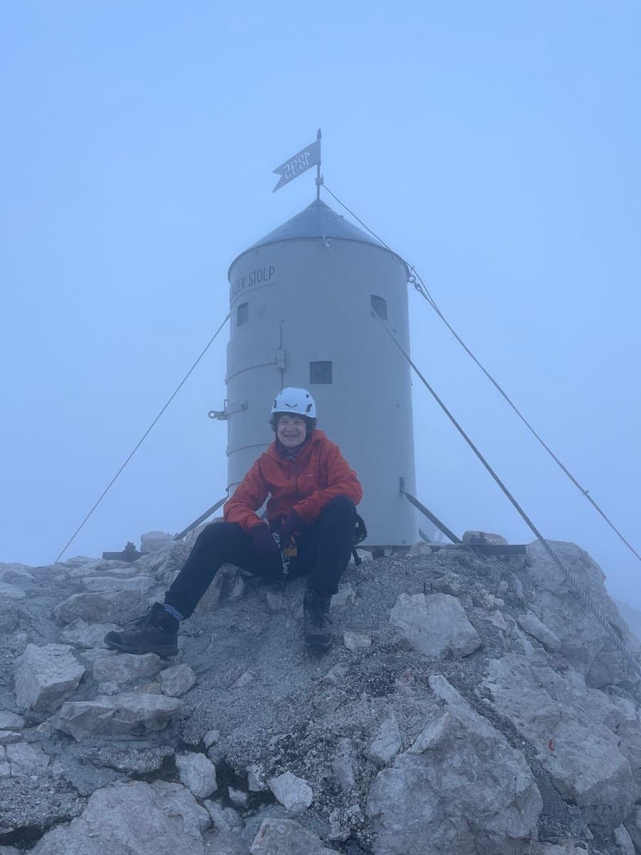 Hiker sitting on rocky mountain summit in front of metal tower in fog