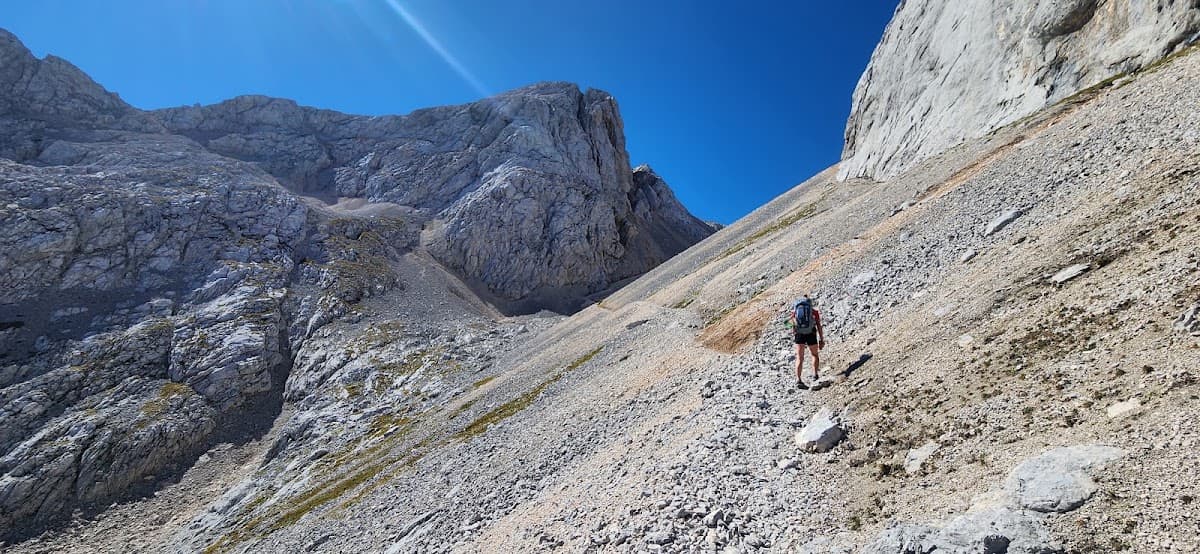 Hiker walking up a steep rocky mountain trail under a clear blue sky