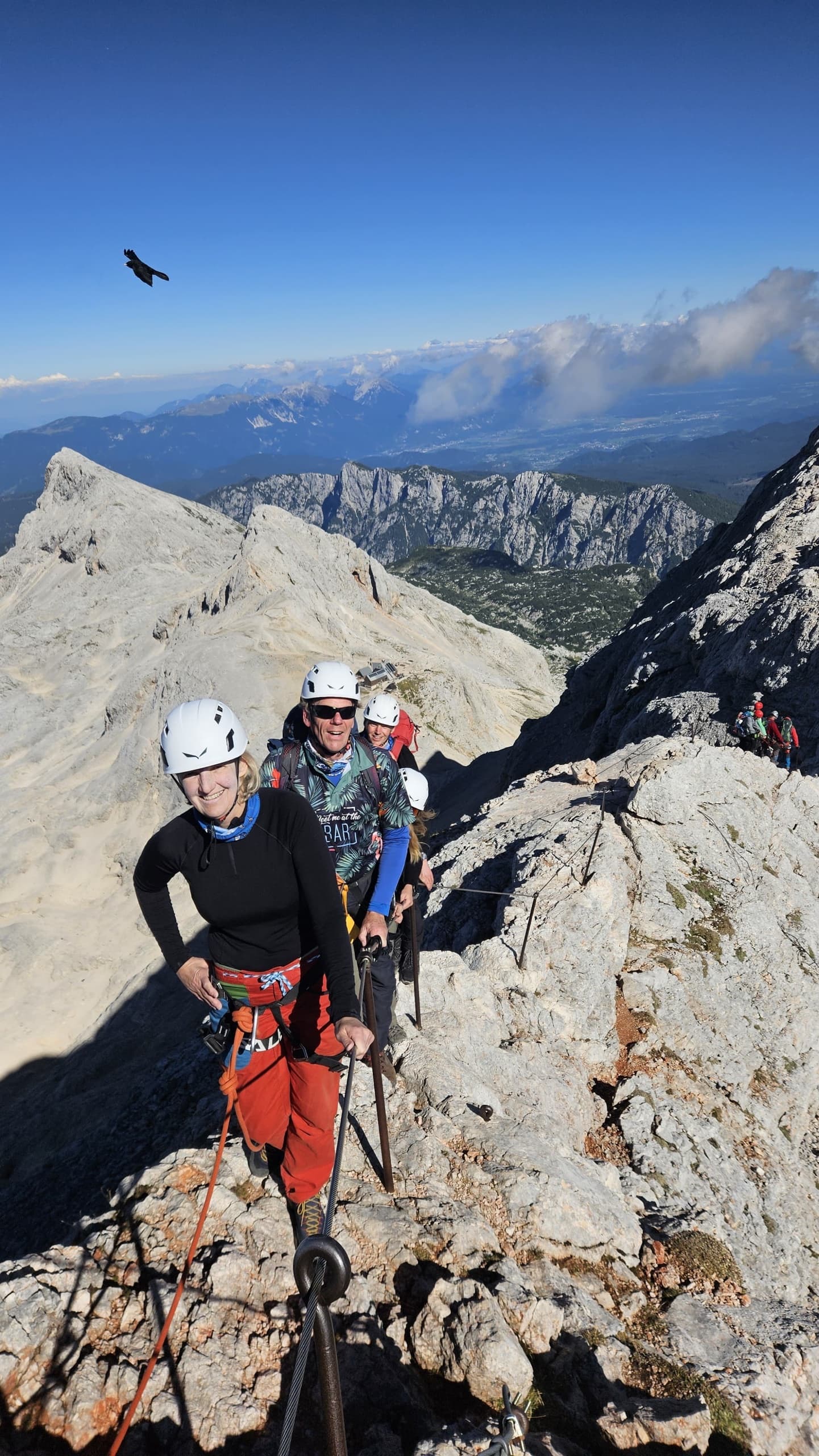 Climbers on a rocky mountain ridge with safety cable above clouds