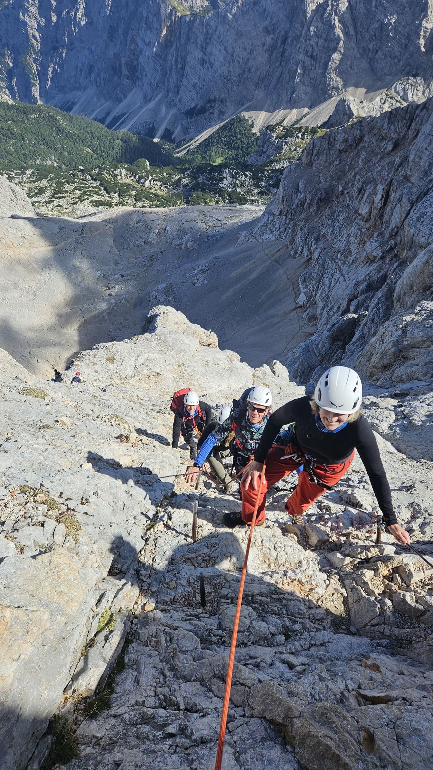 Roped climbers ascending a steep limestone mountain slab with safety cables