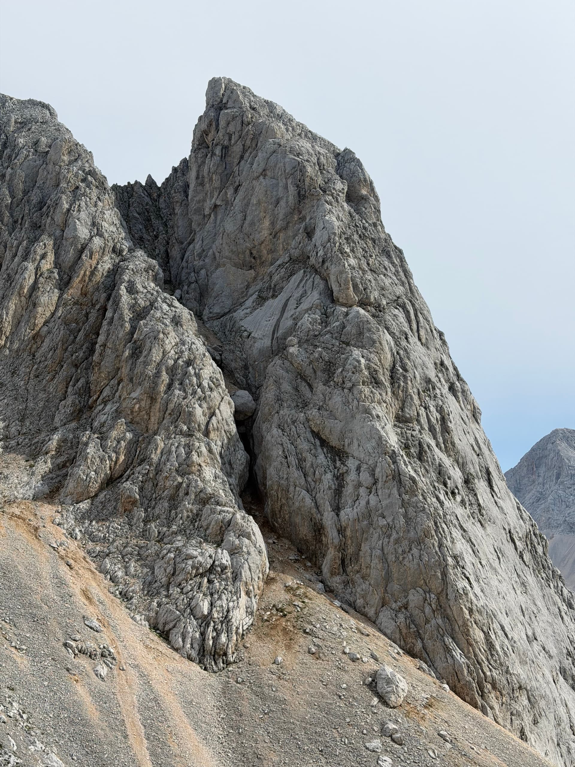 Jagged limestone rock formations and steep mountain peaks against a clear sky