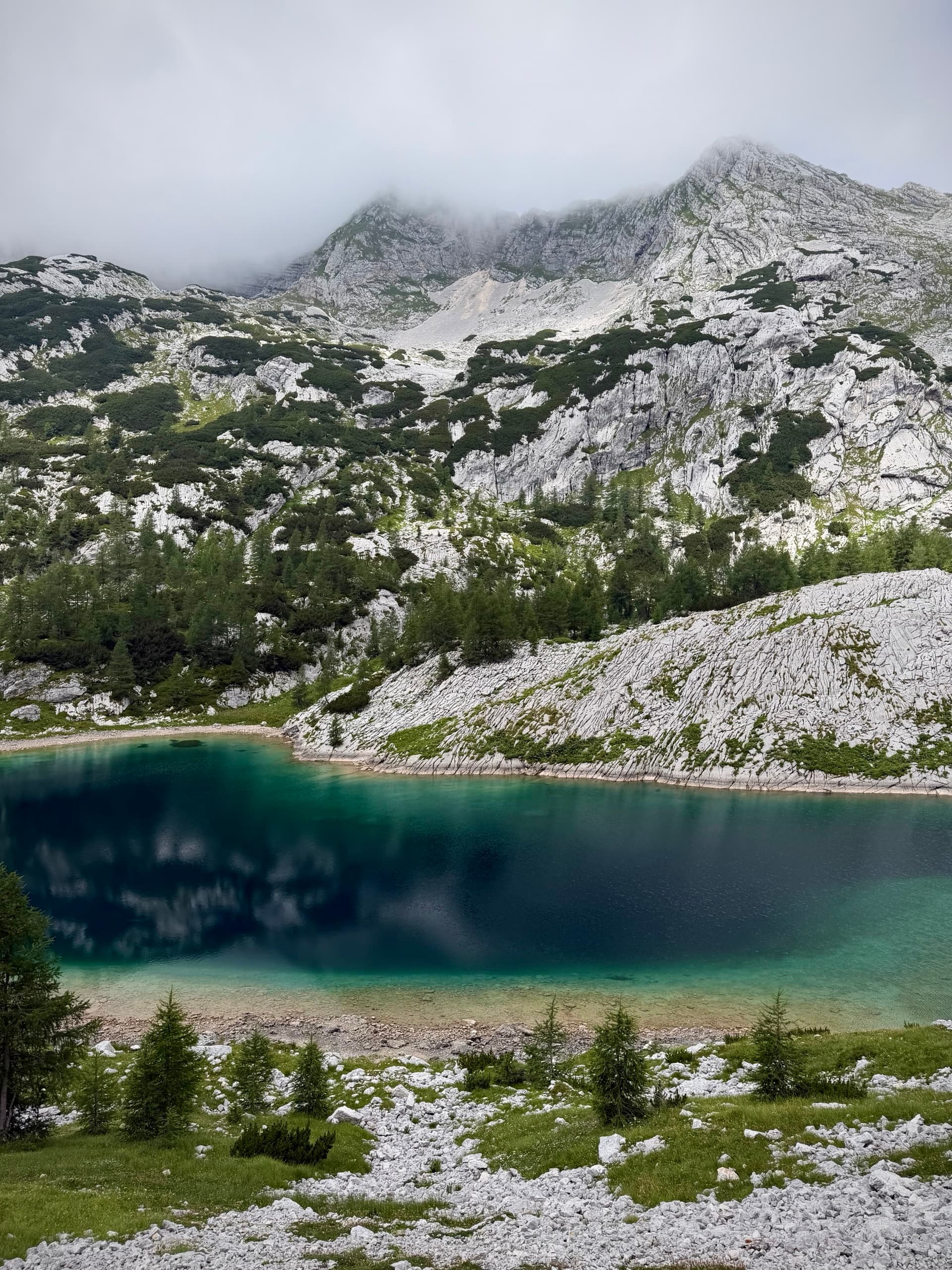 Turquoise alpine lake below rocky limestone ridge and cloudy mountain peaks