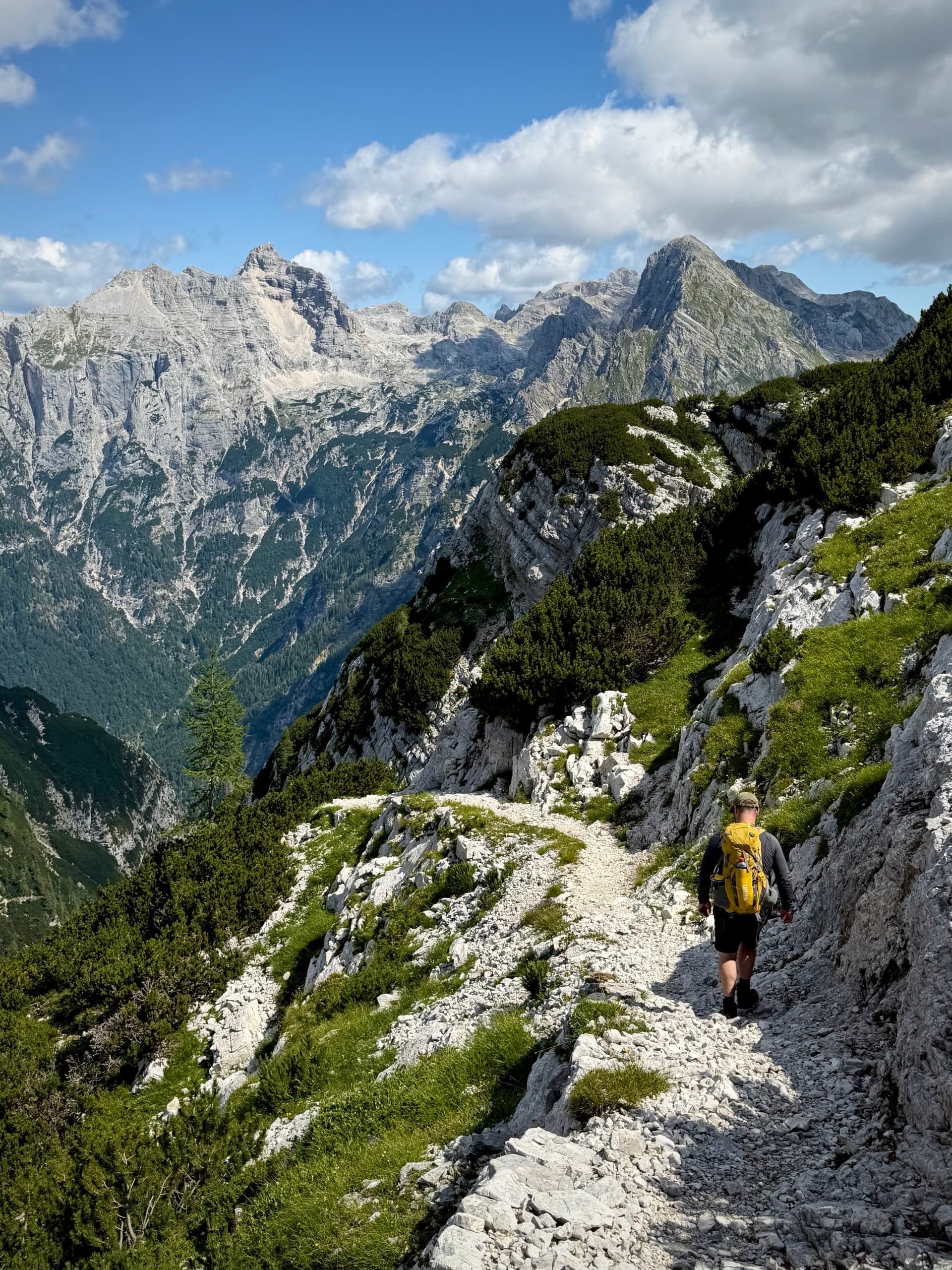 Hiker with yellow backpack on rocky mountain ledge path below peaks