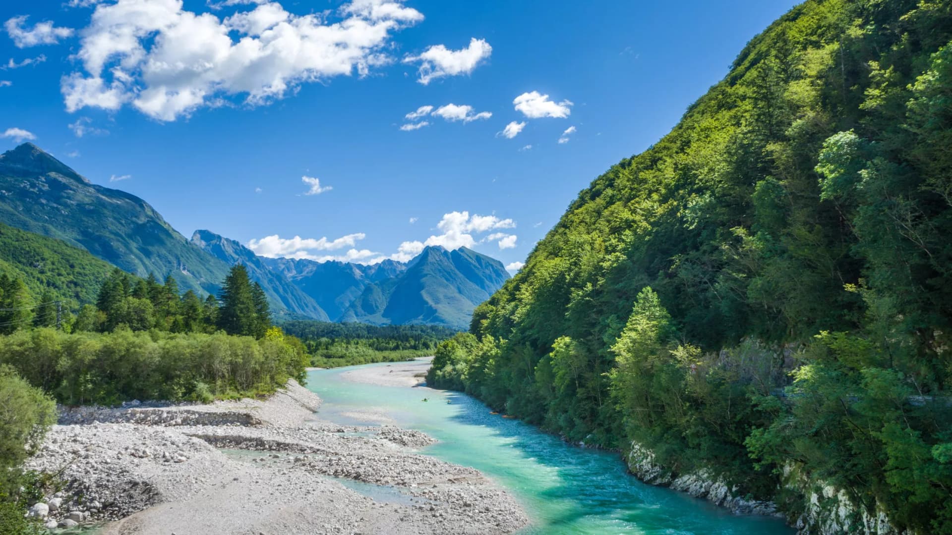 Kayaking on turquoise Soca River in Bovec valley with rocky banks and lush green mountains.