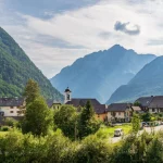 Panorama with buildings, main Road and Parish Church inside Mountain Landscape of Village Log pod Mangartom. Bovec, Slovenia, Europe.